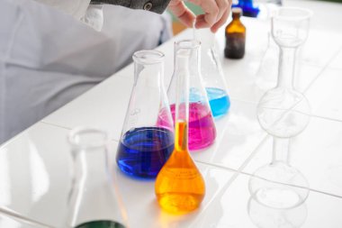 Kız laboratuvar teknisyeni laboratuvarda çeşitli sıvıları mataralarda karıştırıyor.