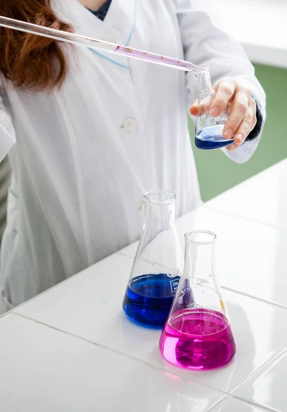 girl lab technician mixes various liquids in flasks in a laboratory
