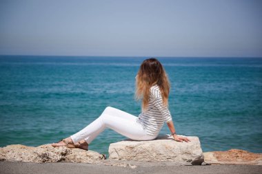 deniz kenarında bir taş üzerinde oturan mutlu Avrupa kız