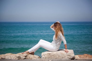 deniz kenarında bir taş üzerinde oturan mutlu Avrupa kız