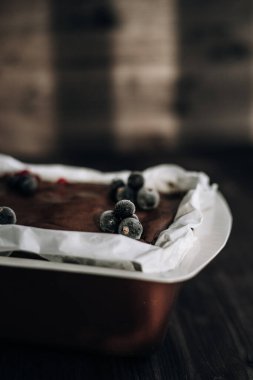 Kahverengi bir küfte donmuş kuşüzümü ve koyu arkaplanda beyaz parşömenle süslenmiş kek.