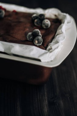 Kahverengi bir küfte donmuş kuşüzümü ve koyu arkaplanda beyaz parşömenle süslenmiş kek.