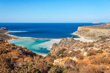 Gezgin bir sırt çantası ile bir kaya üzerinde duruyor ve Balos plaj, Crete, Greec panorama adlı görünüyor