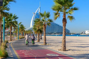 Dubai, Birleşik Arap Emirlikleri 'ndeki Kite Sahili boyunca palmiye ağaçlarıyla kaplı bisiklet yolu. Manzaralı bir sahil yolu bisiklet, koşu ve deniz manzarası ile popüler.