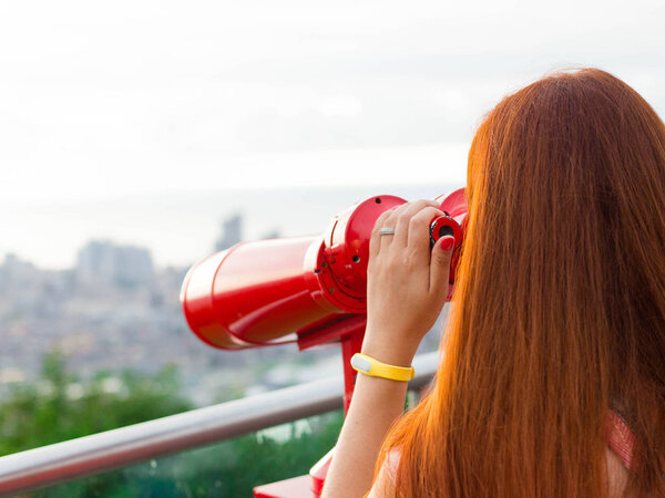 Young woman looking through public binoculars
