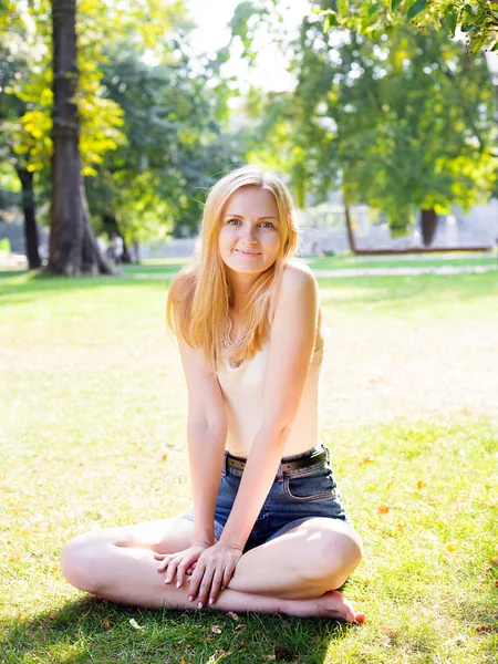 Chica sonriente sentada en la hierba verde al aire libre. Mirando la cámara. Naturaleza al aire libre — Foto de Stock