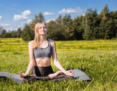 Kollarını açarak ve uzun sarı saçları ile genç erkek yeşil doğada yoga poz rahatlatır