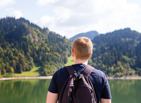Νέοι πεζοπόρος με σακίδιο στέκεται δίπλα στη λίμνη του βουνού και κοιτάζοντας την απόσταση, να χαλαρώσετε Ενοικιαζόμενα — Φωτογραφία Αρχείου