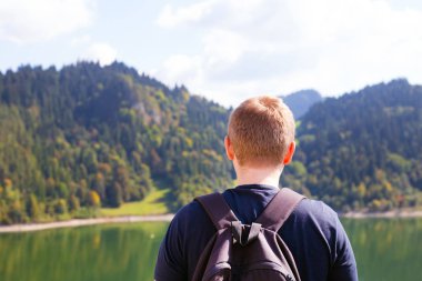 Dağ göl kenarında duran ve mesafe, seyir sırt çantası ile genç hiker sakin tatil