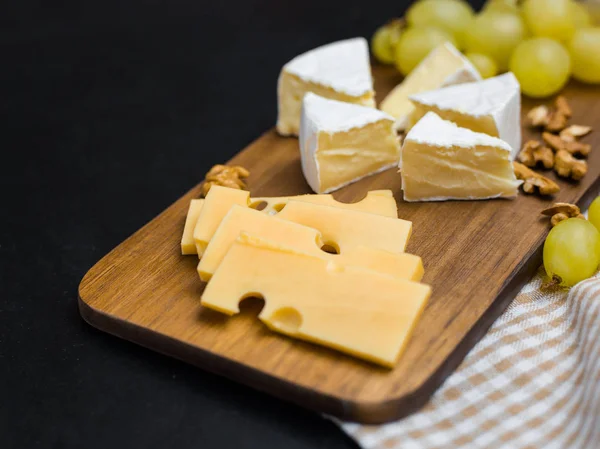 Rebanada de queso, nueces y uvas en tabla de cortar de madera. Queso Camembert y queso edam. Comida para el vino y romántico — Foto de Stock
