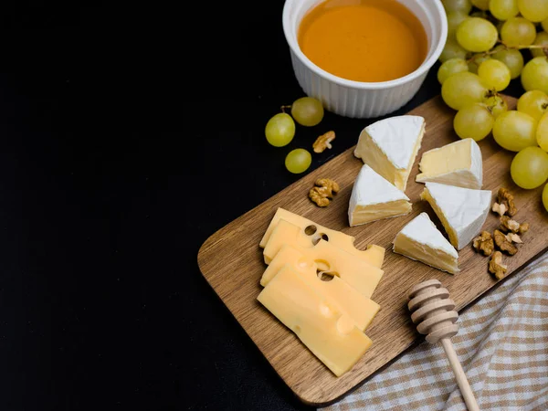 Rebanada de queso, nueces, miel y uvas en tabla de cortar de madera. Queso Camembert y queso edam con tela a cuadros. Comida para el vino y romántico — Foto de Stock