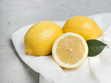 Gri arka plan üzerinde beyaz kumaş ile bütünleşmiş ve dilimlenmiş limon. Organik taze narenciye, kopya alanı.