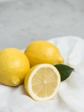 Gri arka plan üzerinde beyaz kumaş ile bütünleşmiş ve dilimlenmiş limon. Organik taze narenciye, kopya alanı.