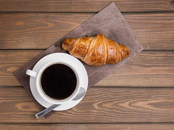 Taza de café y croissant sobre fondo de madera en la mesa. Desayuno perfecto por la mañana. Estilo rústico, vista superior — Foto de Stock