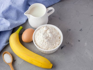 Gri arka plan üzerinde muz kek için malzemeler. Tahta Kaşık, Muz, Yumurta, Süt