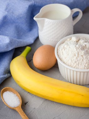 Gri arka plan üzerinde muz kek için malzemeler. Tahta Kaşık, Muz, Yumurta, Süt