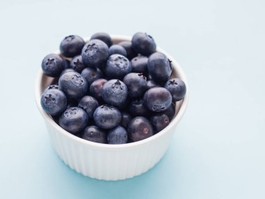 Mavi parlak arka plan üzerinde beyaz kase taze olgun yaban mersini