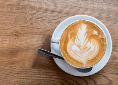 Ahşap masa, beyaz seramik fincan, üst görünümü üzerinde latte sanat ile kapuçino bir fincan. Cafe kültürü.