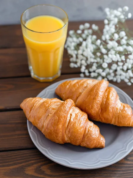 Pyszne śniadanie z rogalikami, kwiatami i sokiem, dzień dobry. Kieliszek orzeźwiającego soku owocowego pomarańczy — Zdjęcie stockowe