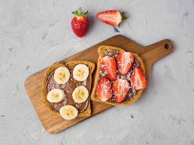 Ahşap bir tahta üzerinde çikolata ve meyve ile tost. Çilek ve muz taş mutfak masa arka plan üzerinde. Üstte görüntü