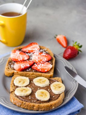 Gri bir tabakta çikolata ve meyve ile tost. Çilek ve muz taş mutfak masa arka plan üzerinde. Üstte görüntü