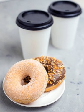 Gri beton arka plan üzerinde renkli çörekler ve beyaz kağıt bardak, yakın, üst görünümü. Fırın konsepti, taze hamur işleri, lezzetli kahvaltı, fast food