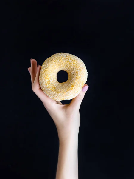 Женщина держит сладкий сахарный пончик на черном фоне — стоковое фото