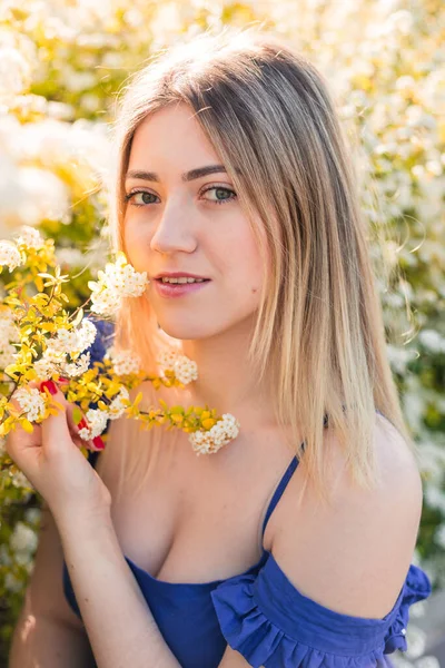 Αισθησιακό ήρεμο πορτρέτο της όμορφης hipster γυναίκας σε ανθισμένους θάμνους με λευκά λουλούδια της σπιρέας. Αντιγραφή χώρου. Κομψή ξανθιά γυναίκα σε μπλε φόρεμα στον κήπο — Φωτογραφία Αρχείου