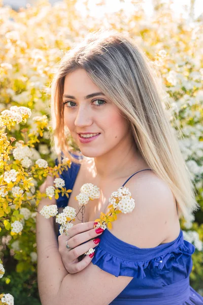 Sensual retrato tranquilo de una hermosa mujer hipster en un arbusto floreciente con flores blancas de espirea. Copiar espacio. Mujer rubia con estilo en vestido azul en el jardín — Foto de Stock