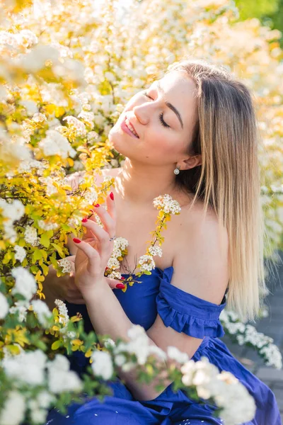 Sensual calm portrait of beautiful hipster woman in blooming bush with white flowers of spirea. Copy space. Stylish blonde woman in blue dress in garden — Stock Photo, Image