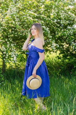 Çiçekli çalılıklarda beyaz spirea çiçekleriyle güzel hippi kadın portresi. Uzayı kopyala Bahçede hasır şapkalı, mavi elbiseli şık sarışın kadın.