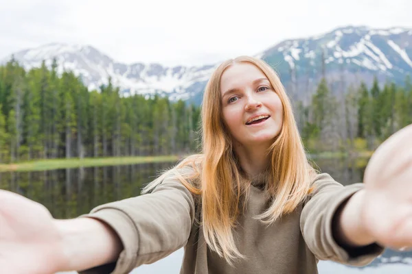 女の子の観光客は山の湖で自撮り。カメラと笑顔を見て。旅行と積極的な生活の概念。屋外 — ストック写真