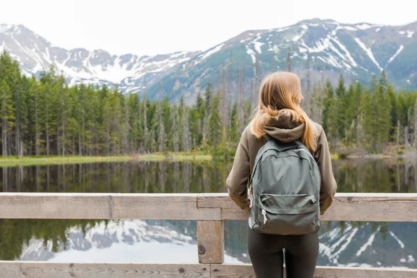 Chica joven rubia de pie junto al lago de montaña en el bosque. Viajes y concepto de vida activa. Al aire libre — Foto de Stock