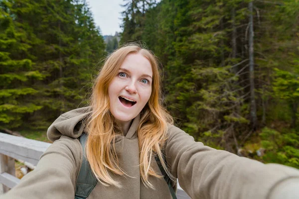 Belle jeune femme randonneuse prenant selfie dans la forêt de montagne. En regardant la caméra et sourire. Concept de voyage et de vie active. À l'extérieur — Photo