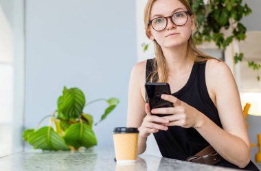 Kafede cep telefonu kullanan ve sosyal ağlarda mesajlaşan güzel bir kadın, kahve içen serbest çalışan bir kadın. Konsepti kaldır.