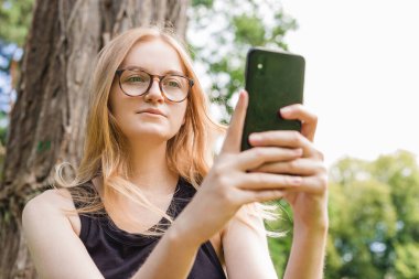 Güzel genç hippi kadın parkta selfie çekiyor. Kameraya bakıp gülümse. Seyahat ve aktif yaşam konsepti.