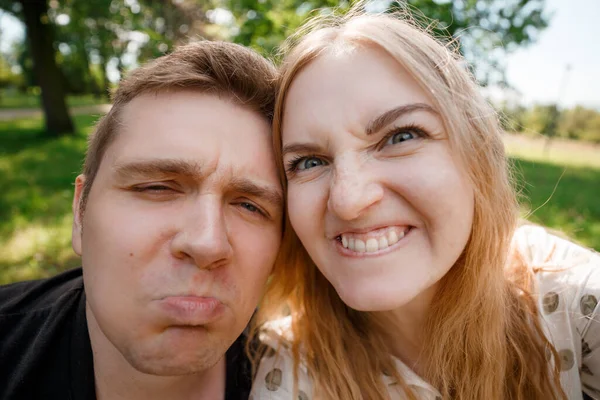 Dva milenci dělají legrační selfie, portrét veselých smějících se mladých lidí. Pár roztomilých hipsterů se prochází v parku. Emoční výraz obličeje. Krásný slunečný den. — Stock fotografie