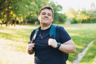 Kırsalda duran sırt çantalı 30 'lu yaşlarda sarışın bir adam. Gezgin. Yaz zamanı. Açık havada dikilen sıradan giysili mutlu genç adamın portresi.