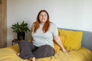 Yatakta oturup kameraya gülümseyen olumlu bir kadın.