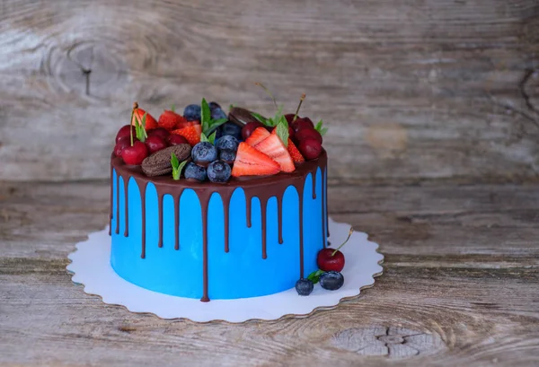 beautiful homemade cake with blue cream cream decorated with cherries, strawberries and blueberries on a wooden table