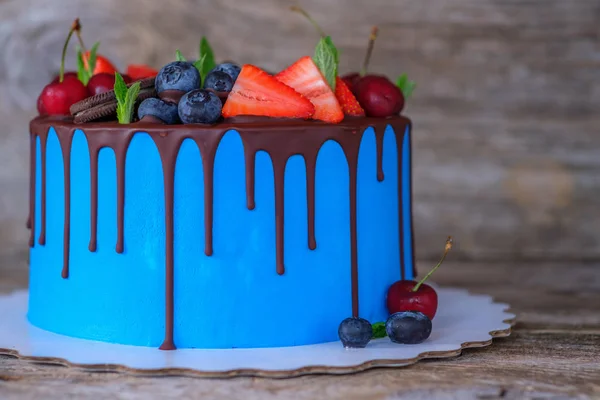 beautiful homemade cake with blue cream cream decorated with cherries, strawberries and blueberries on a wooden table