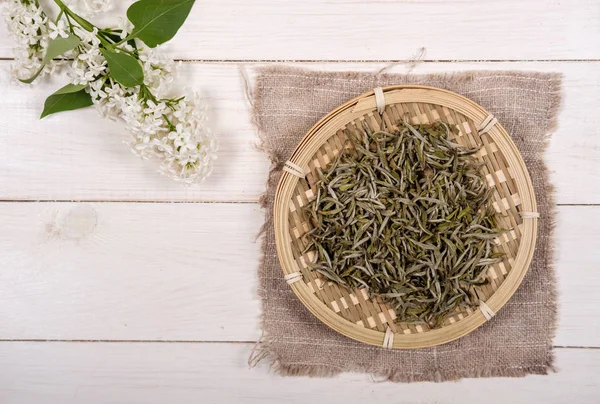 Chinese white tea in bamboo dish and white lilac flowers on wooden background