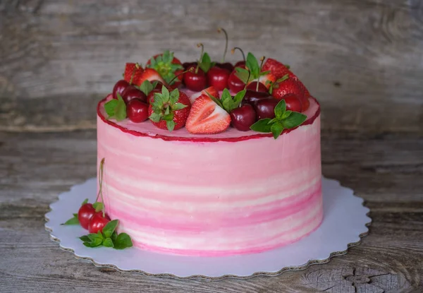 beautiful home cake with pink cream, decorated with cherries and strawberries, on a wooden table