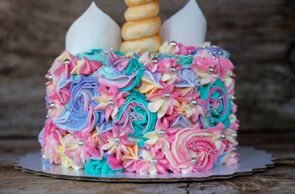 木製テーブルの上のクリーム色の花とユニコーンの形で美しい自家製ケーキ — ストック写真