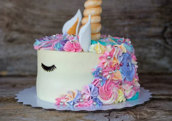 beautiful homemade cake in the form of a unicorn with cream colored flowers on a wooden table