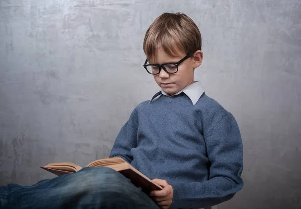 Мальчик в очках читает книгу — стоковое фото