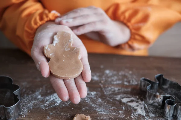 cute European boy in a chef\'s cap and apron prepares ginger cookies in the kitchen at the table