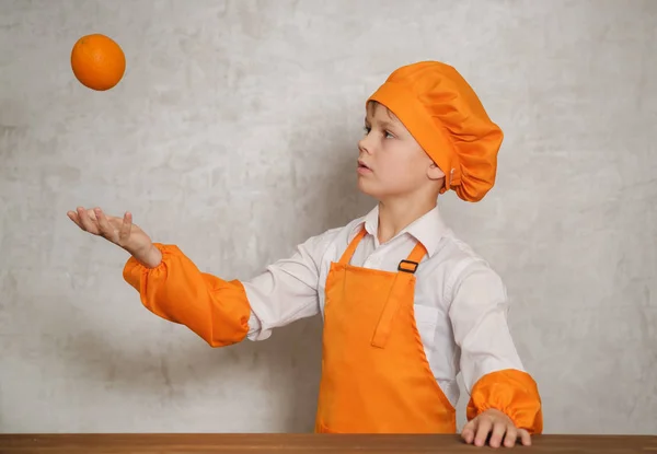 Милый мальчик в оранжевом костюме шеф-повара бросает оранжевый — стоковое фото