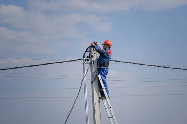 Ingeniero eléctrico realiza cableado en un poste alto de pie en las escaleras. trabajos eléctricos de gran altura. casa podkluchenie a las líneas eléctricas — Foto de Stock