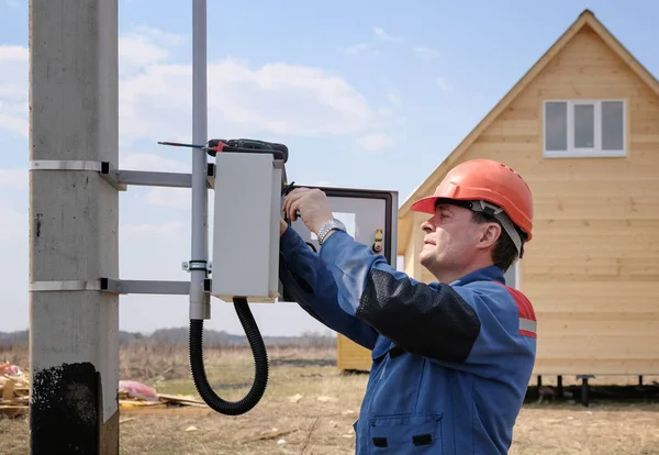 electrician engaged in the installation of electricity meter on the support of power lines . the process of the electrician. side view of the house